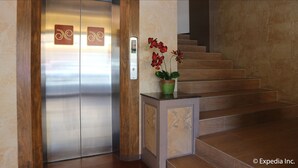 Een lift met een houten frame en een rode orchidee in een pot op een klein tafeltje naast een trap.