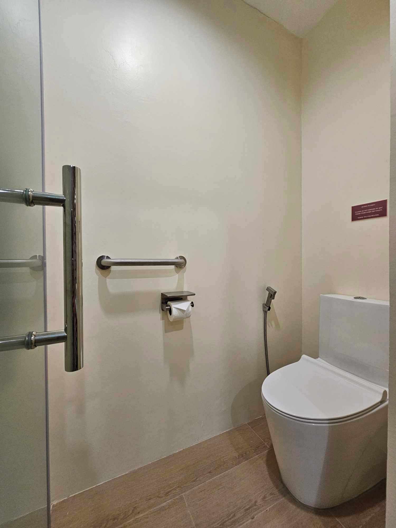 A bathroom with a white toilet, a handrail, and a paper towel dispenser.