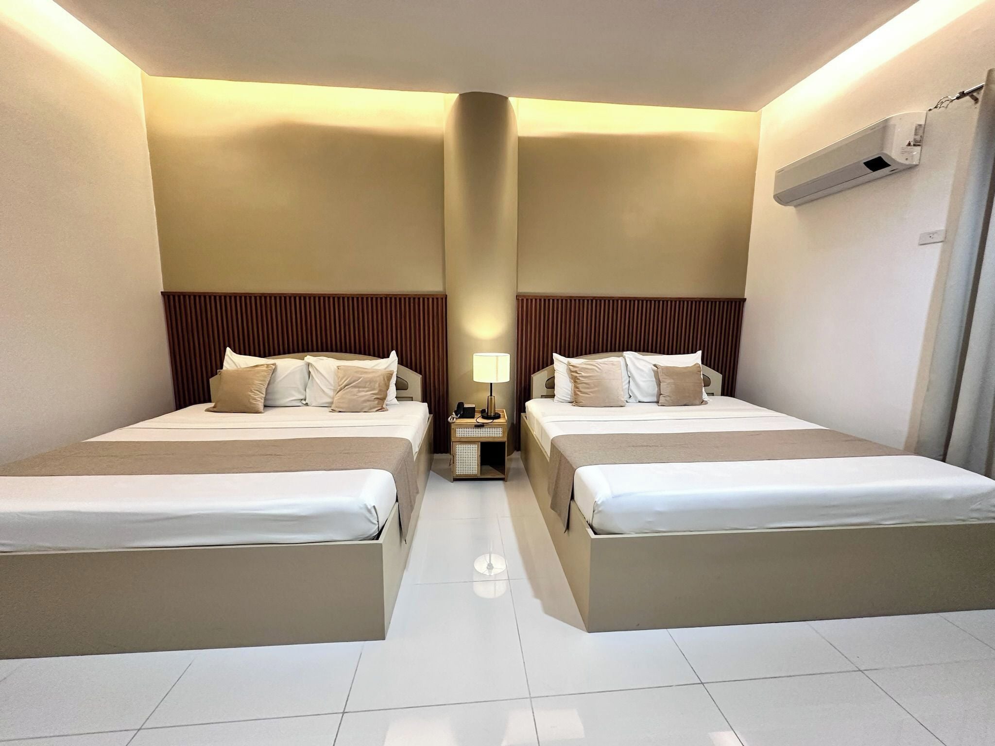 Ein Hotelzimmer mit zwei Betten, einem Nachttisch mit Lampe und einer Klimaanlage an der Wand.