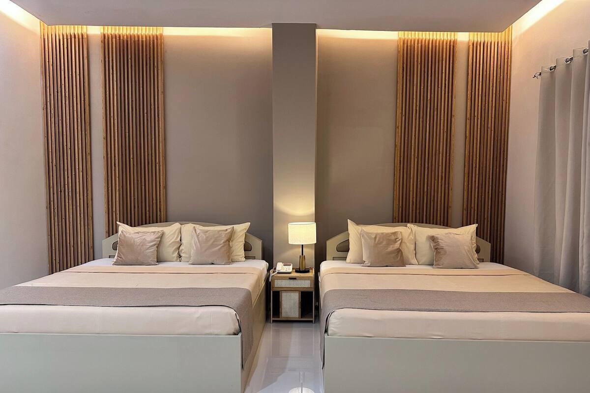 Habitación doble con dos camas, una mesita de noche, una lámpara y un espejo.