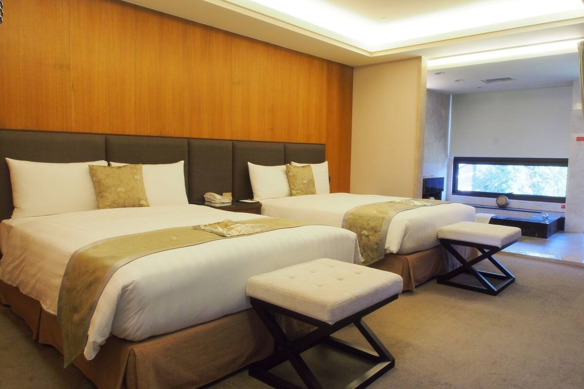 A hotel room with two beds, a TV, and a window.