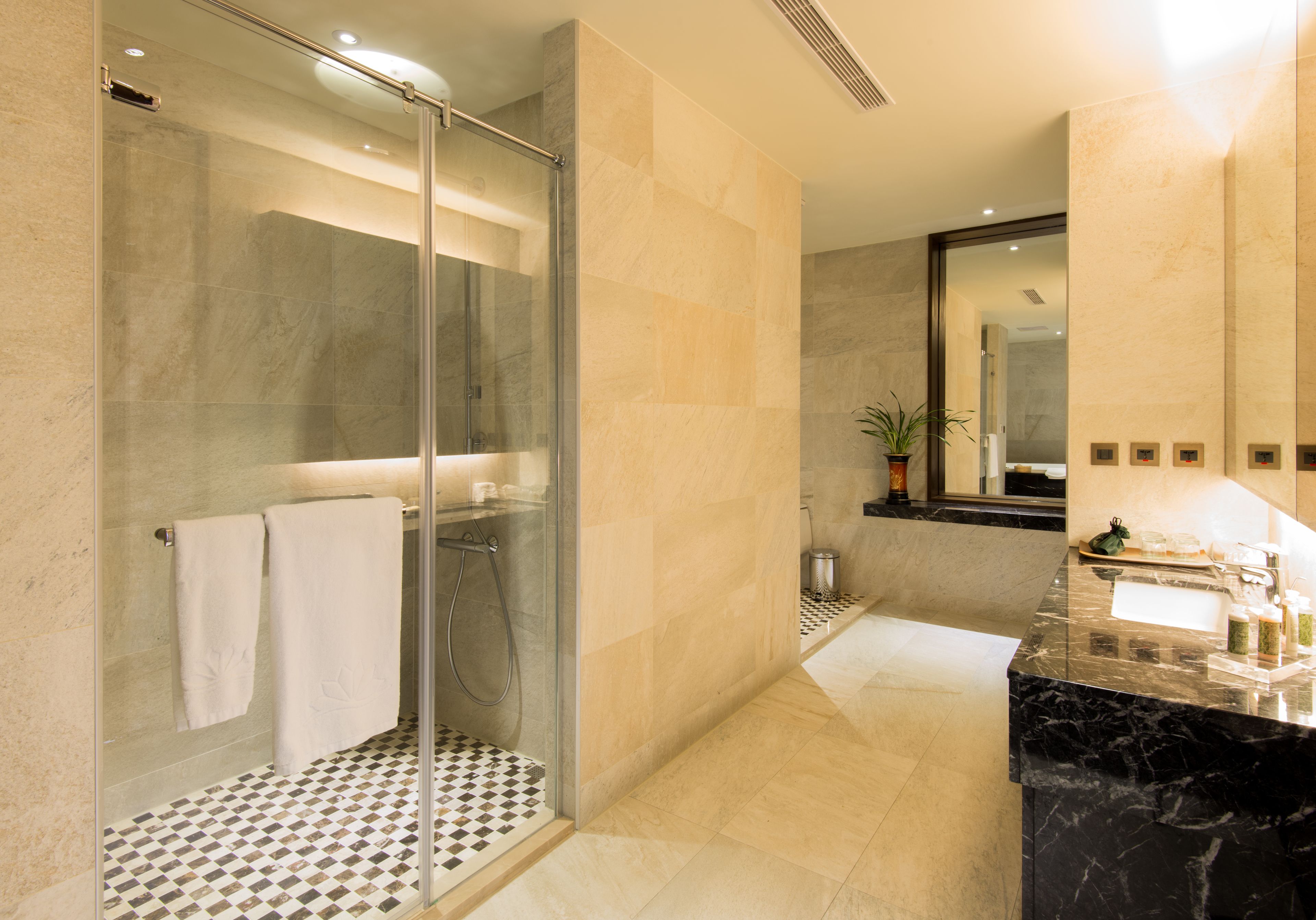 Un baño moderno con ducha envuelta en vidrio, lavamanos de mármol y un piso con diseño de cuadros.