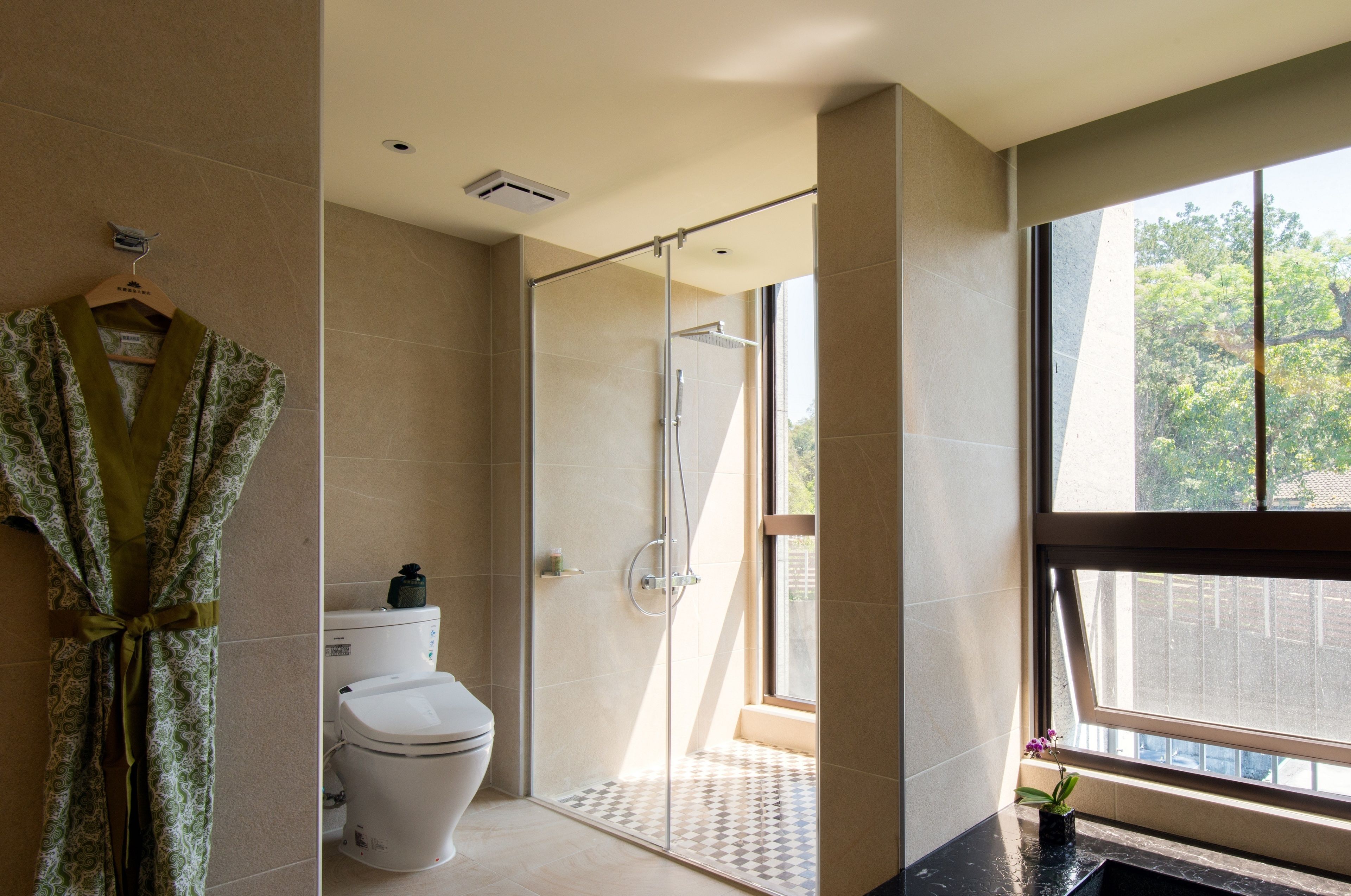 A modern bathroom with a glass-enclosed shower, a toilet, and a large window providing a view of the outdoors.