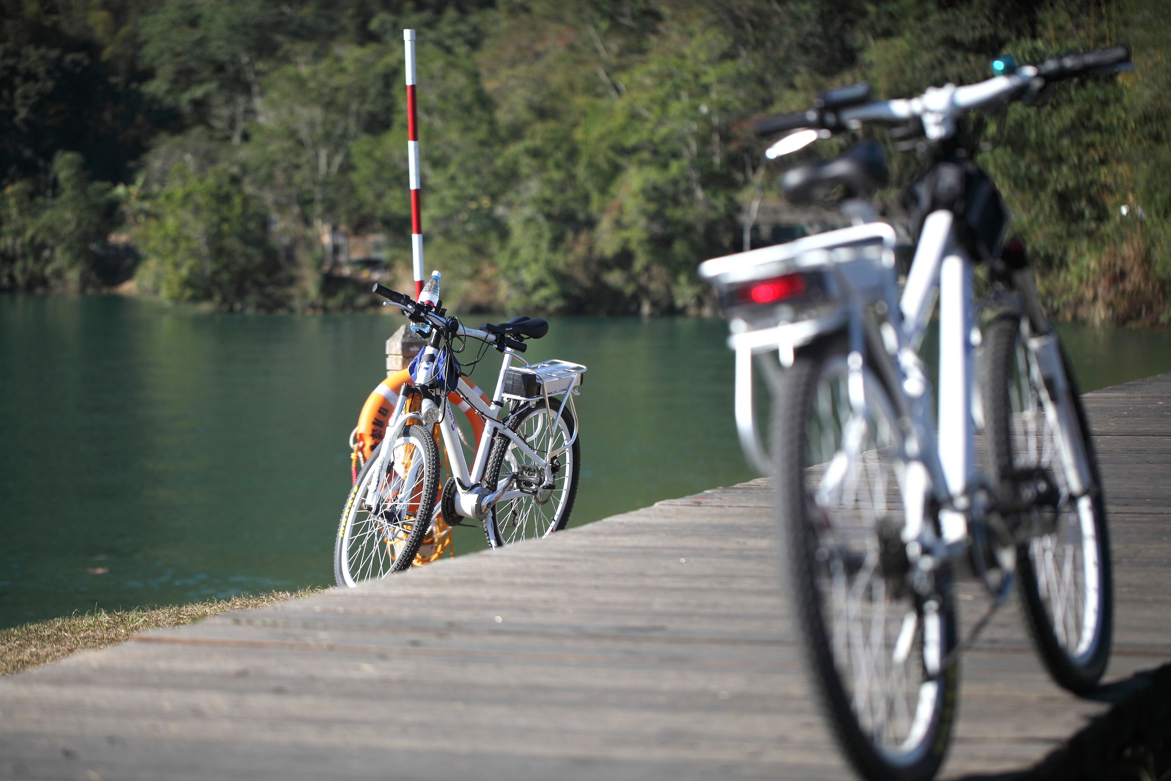 A wooden dock with bicycles parked on it, overlooking a calm lake with trees in the background.