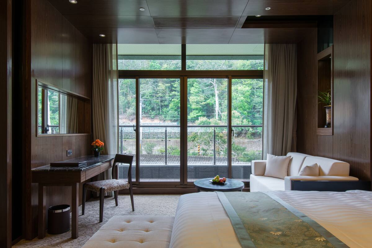 A hotel room with a bed, a desk, a chair, a sofa, and a small table with fruit.