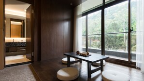A modern room with a wooden floor, a large window with a view of greenery, a dark table, and two round ottomans.