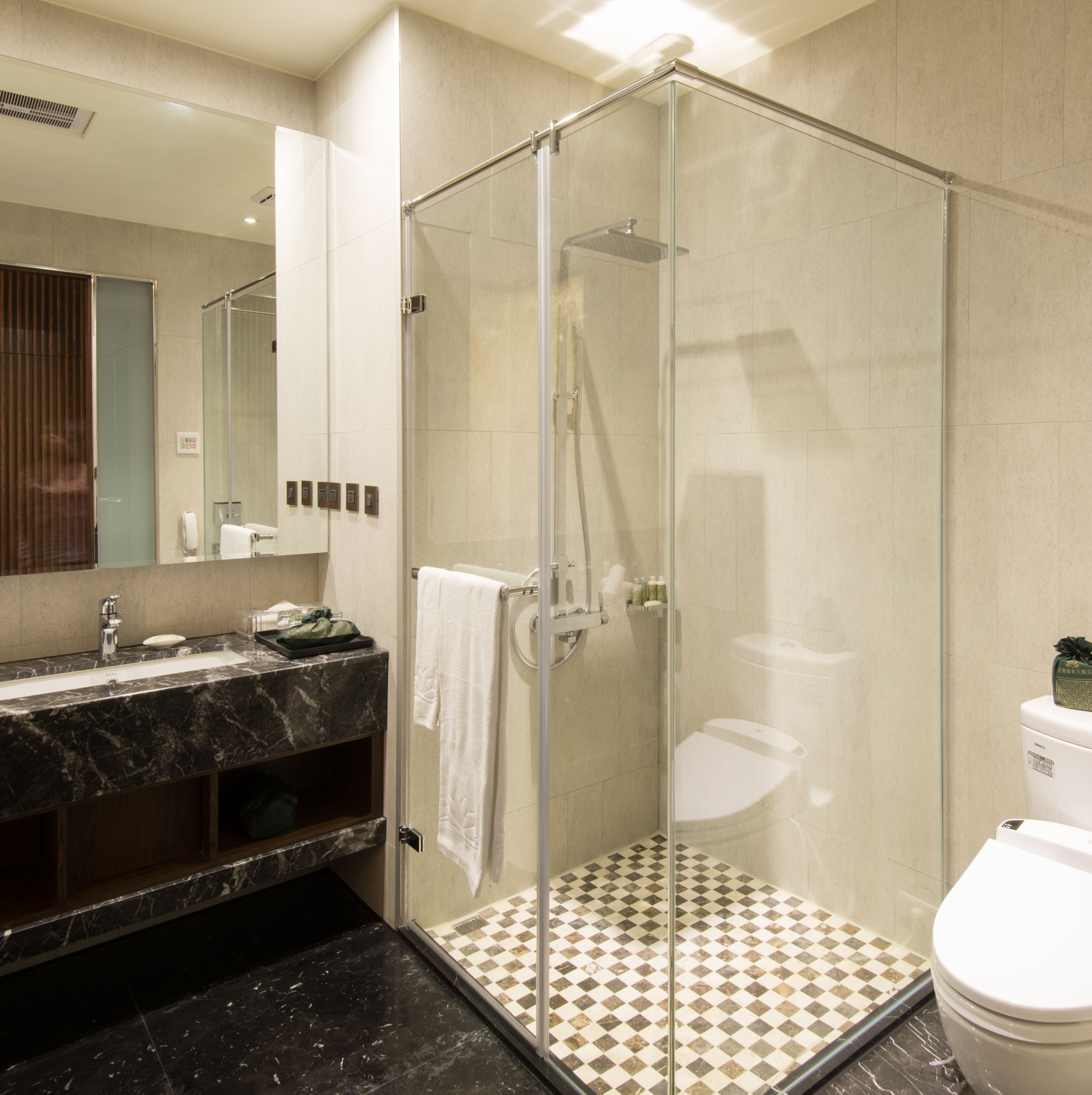 A modern bathroom with a glass-enclosed shower, a marble sink, and a toilet with a checkered floor.