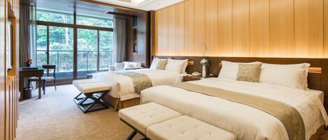 A hotel room with two beds, a desk, and a large window offering a view of trees.
