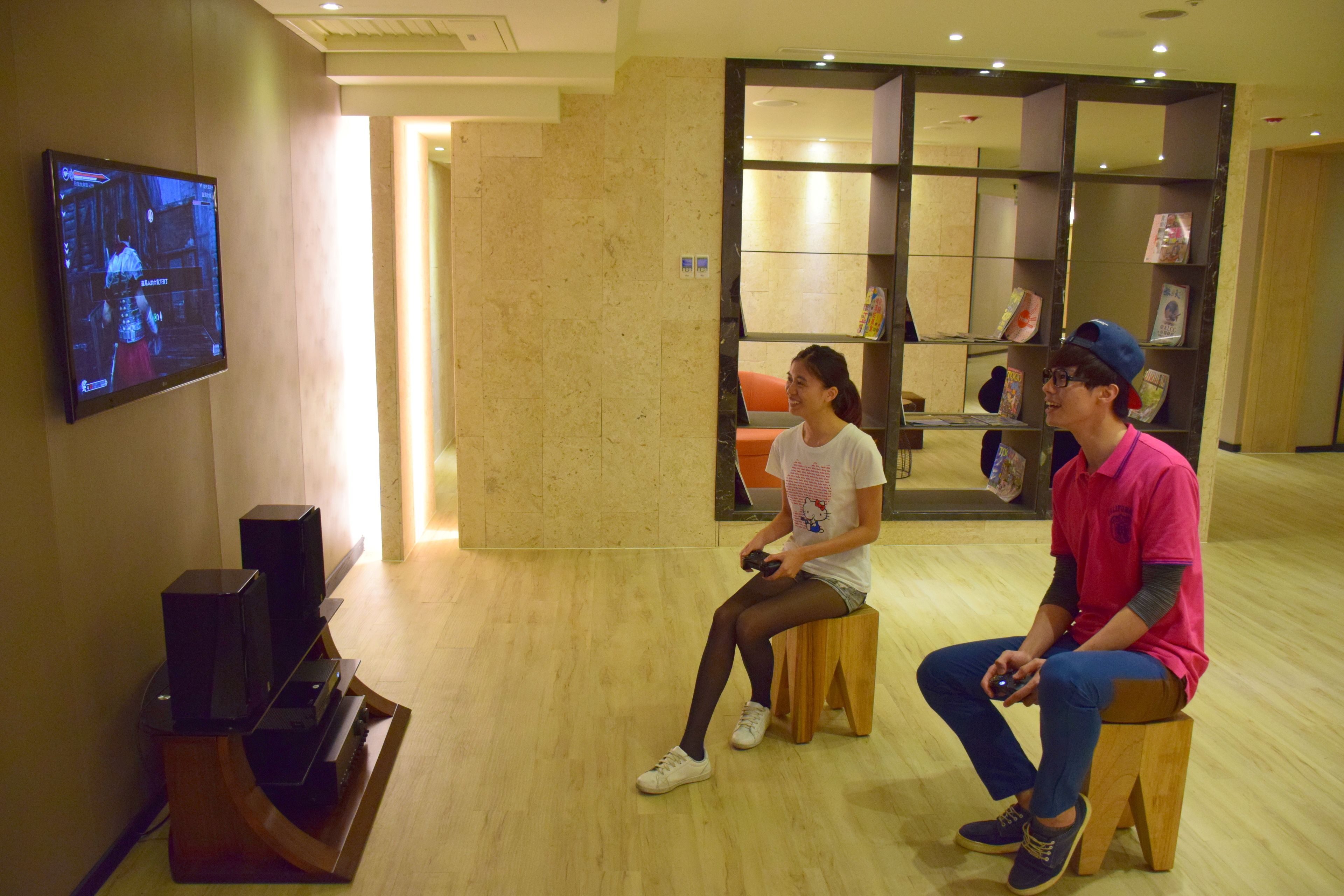 Una habitación con una televisión instalada en la pared, un banco de madera y una estantería con diversos objetos.