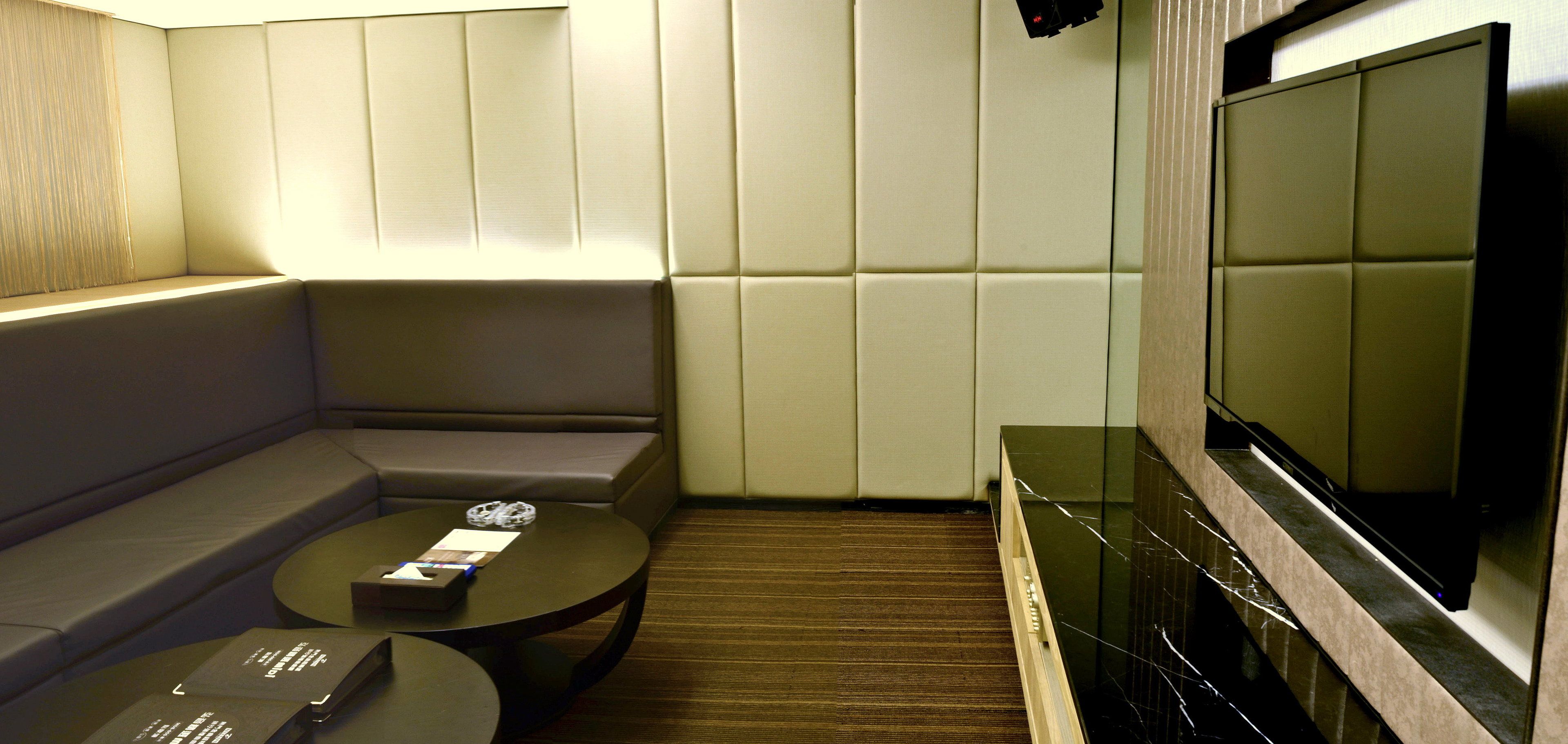 A modern hotel room with a sectional sofa, a small round table, and a flat-screen TV mounted on the wall.