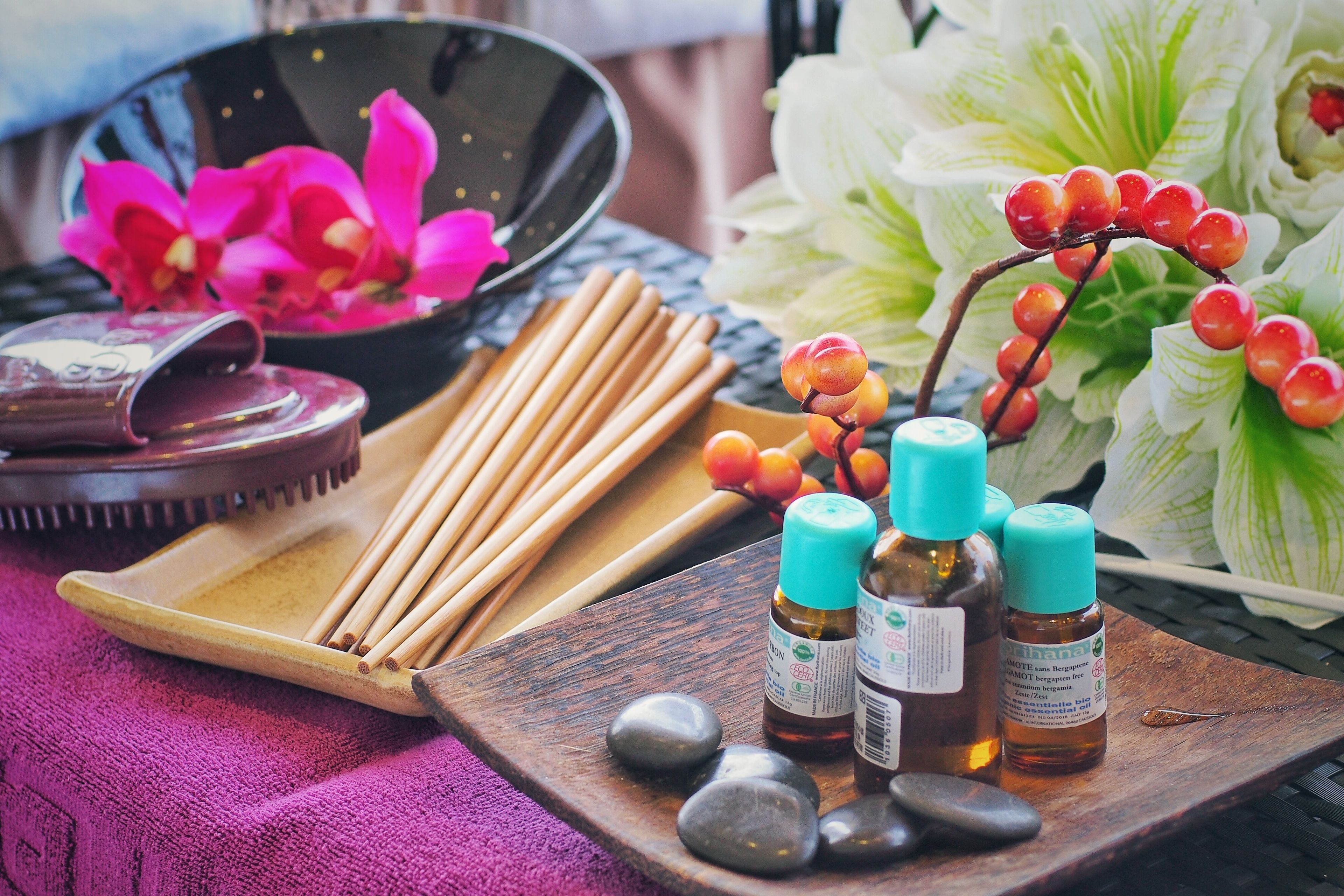 A wooden tray with essential oils, a bowl of pink flowers, and a decorative branch with red berries.