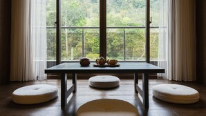 A room with a large window, a table with a teapot and cups, and three round cushions on the floor.