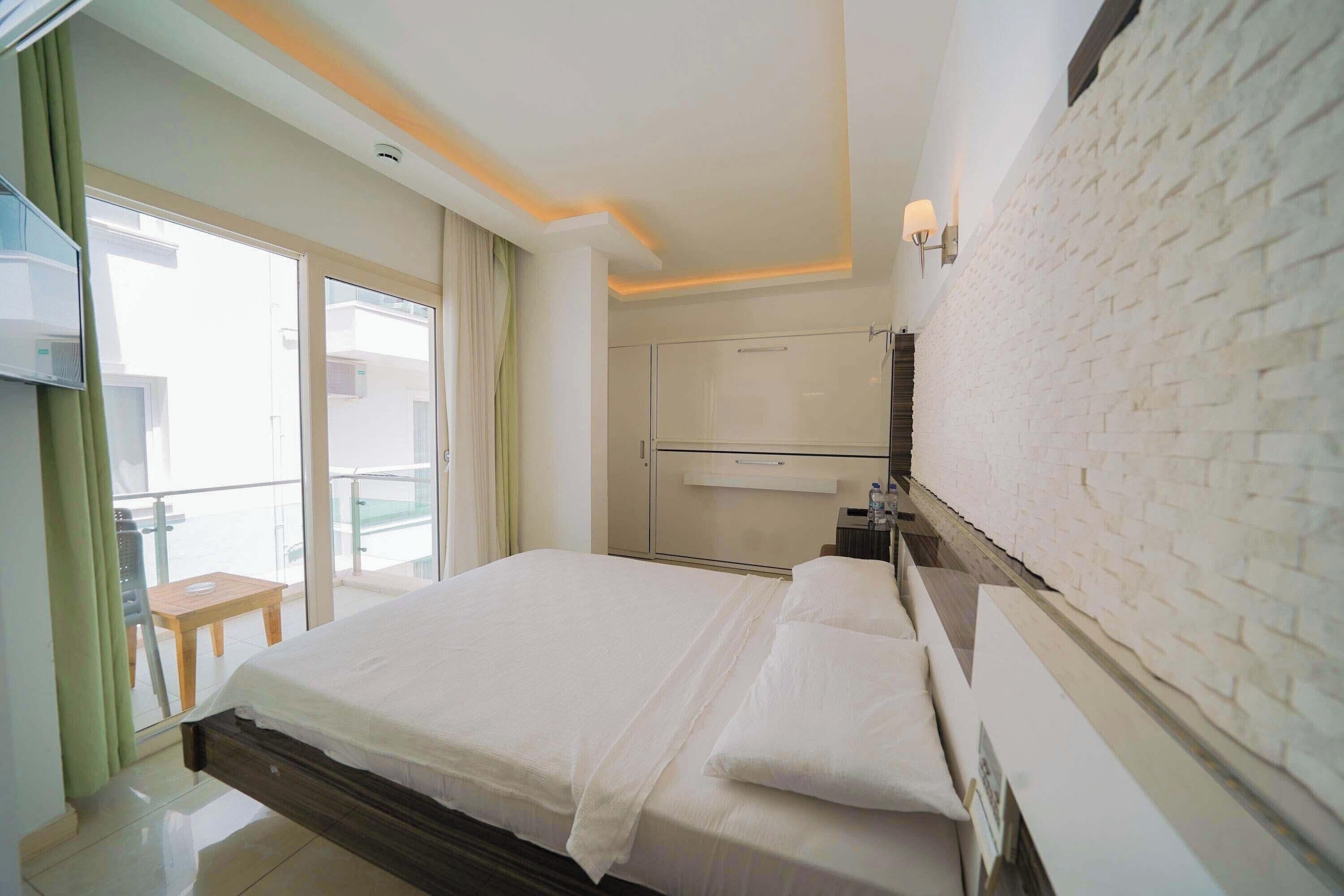 A hotel room with a bed, a wardrobe, a bedside table, and a view of the outside balcony.