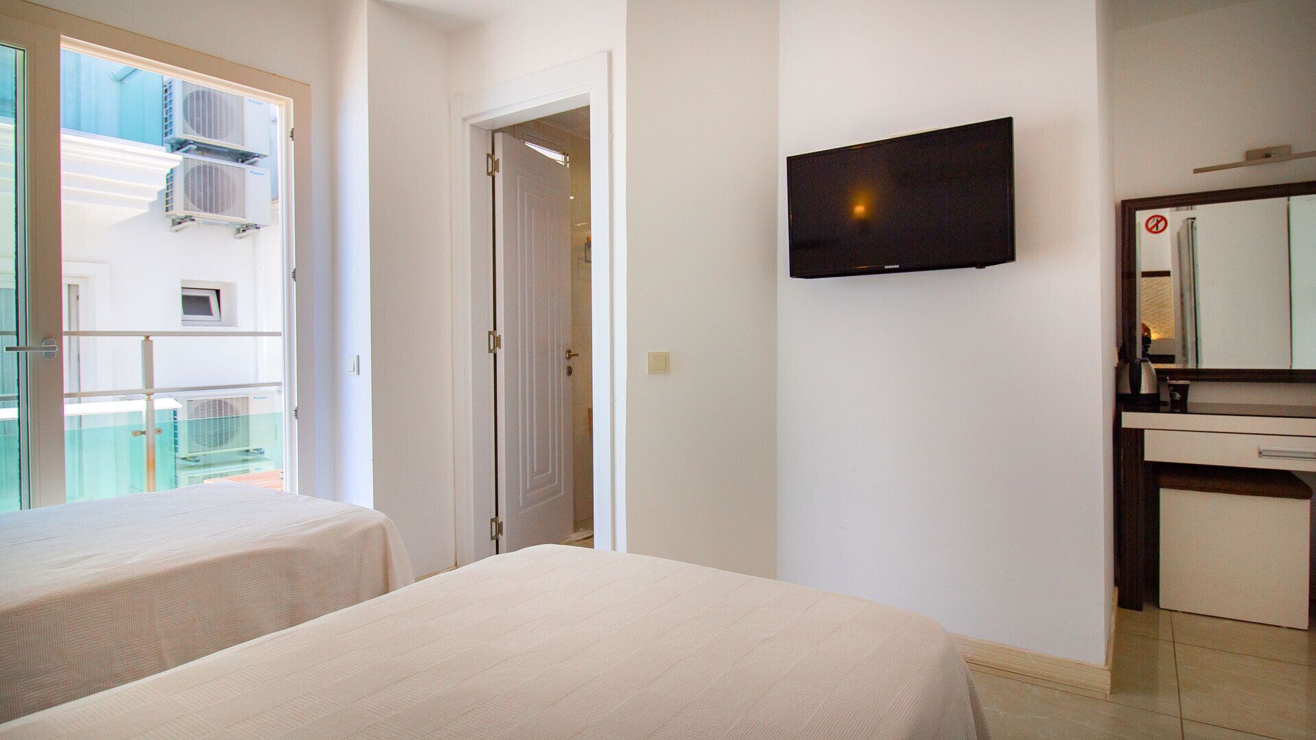 Une chambre d’hôtel avec deux lits, une télévision, une salle de bain avec un miroir et un balcon équipé de climatiseurs.