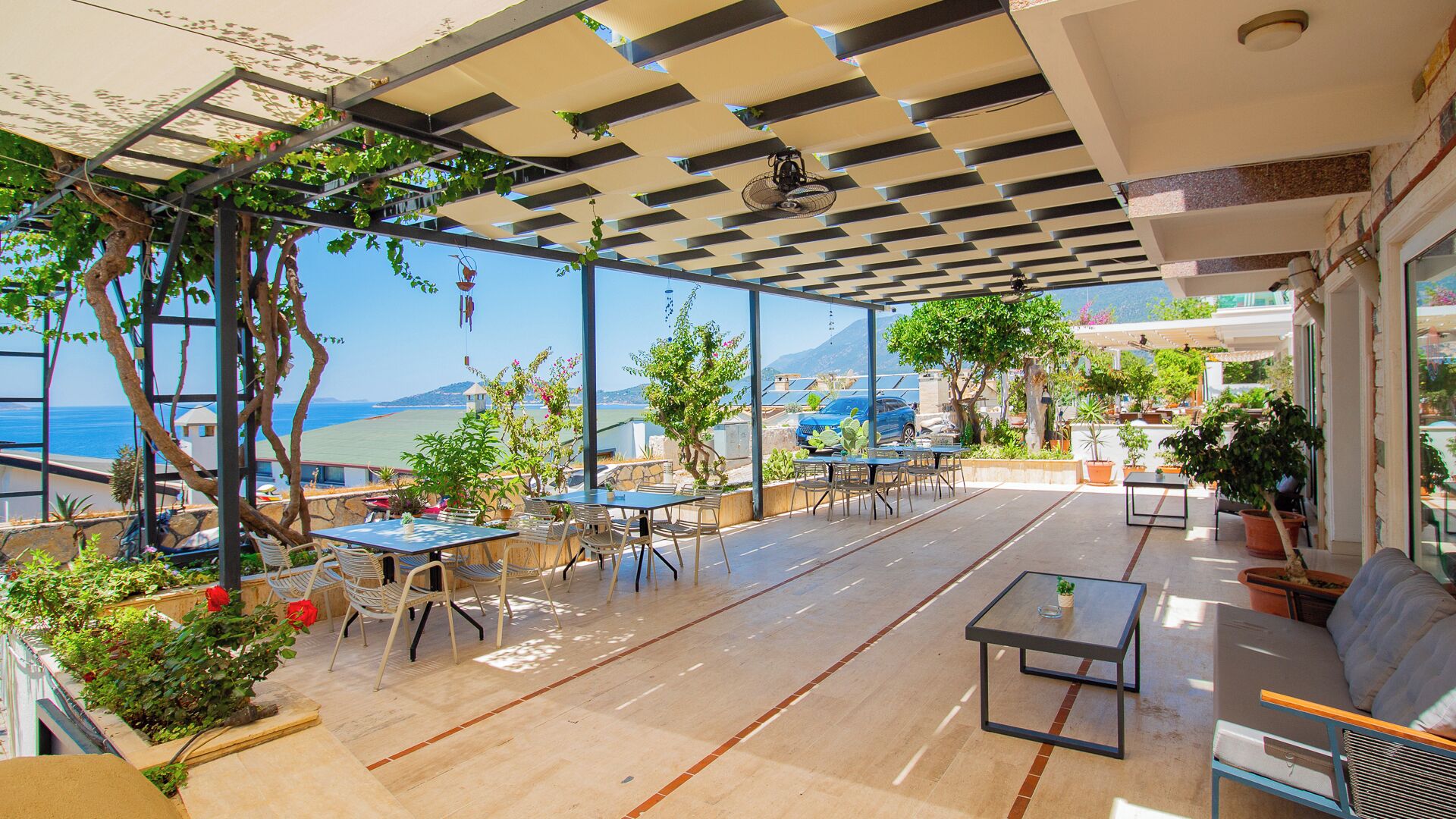 Un'area esterna con tavoli e sedie, piante in vaso e vista sul mare.