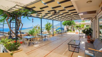 Un'area esterna con tavoli e sedie, piante in vaso e vista sul mare.