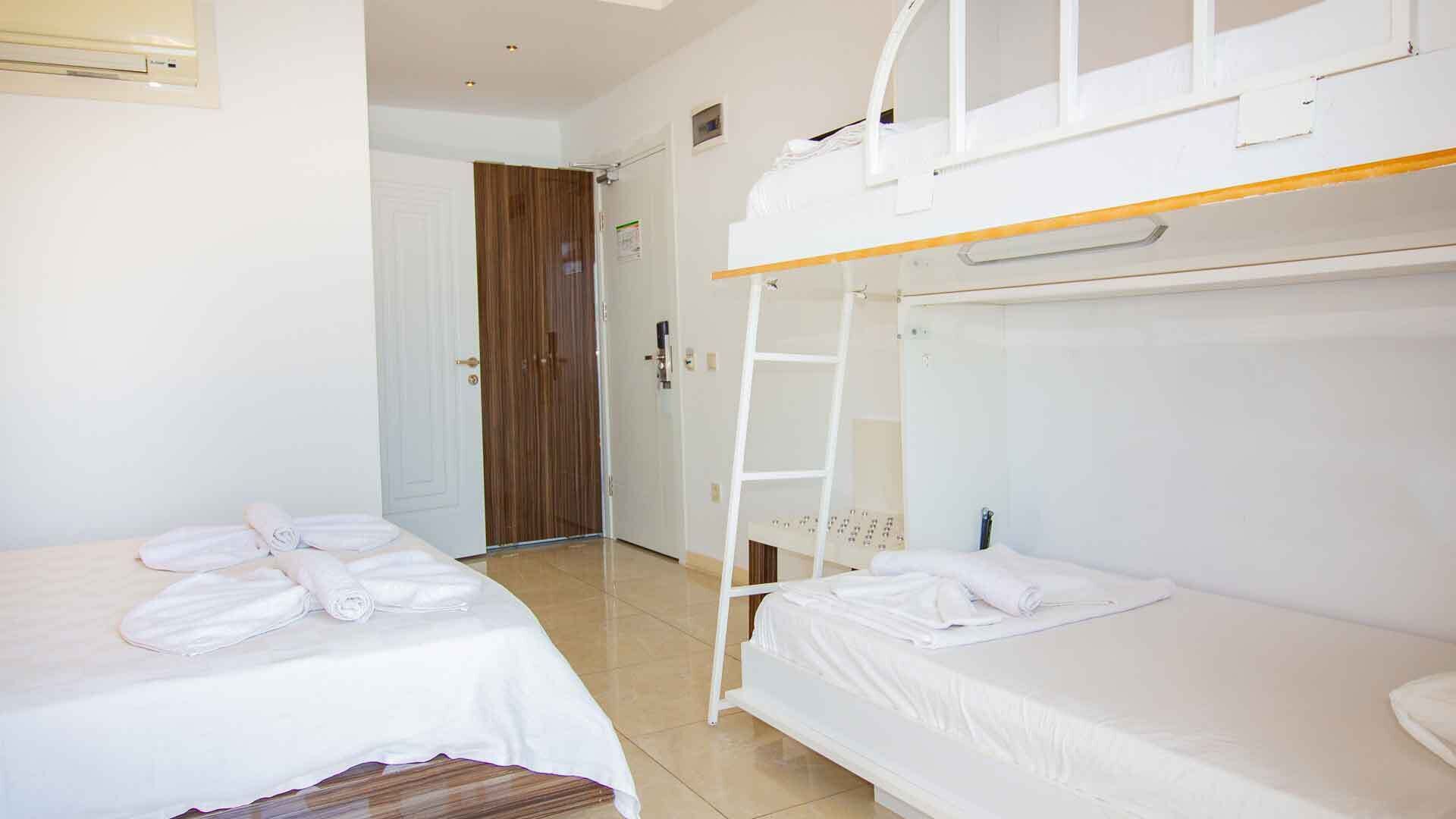 A room with two beds, a bunk bed, a wooden door, and a white wall.
