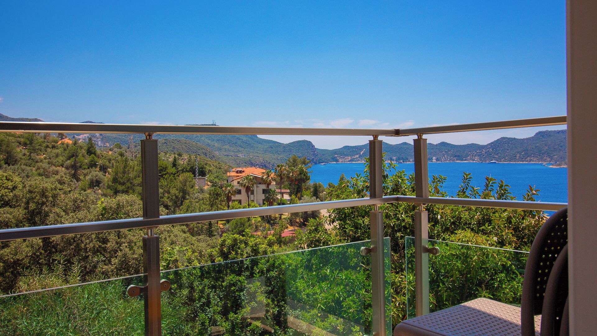 A balcony with a clear view of a coastal landscape, including a body of water and distant hills.