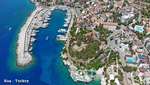 An aerial view of a coastal town with a marina, residential buildings, and a resort area with a pool. - Kas Maki Hotel (Kas)