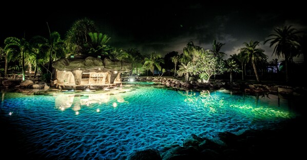 A nighttime pool area with a rock structure and palm trees. - Ohana Resort and Restaurant (Rayong)