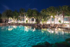 A nighttime resort pool with clear water, palm trees, and resort buildings with balconies. - Ohana Resort and Restaurant (Rayong)