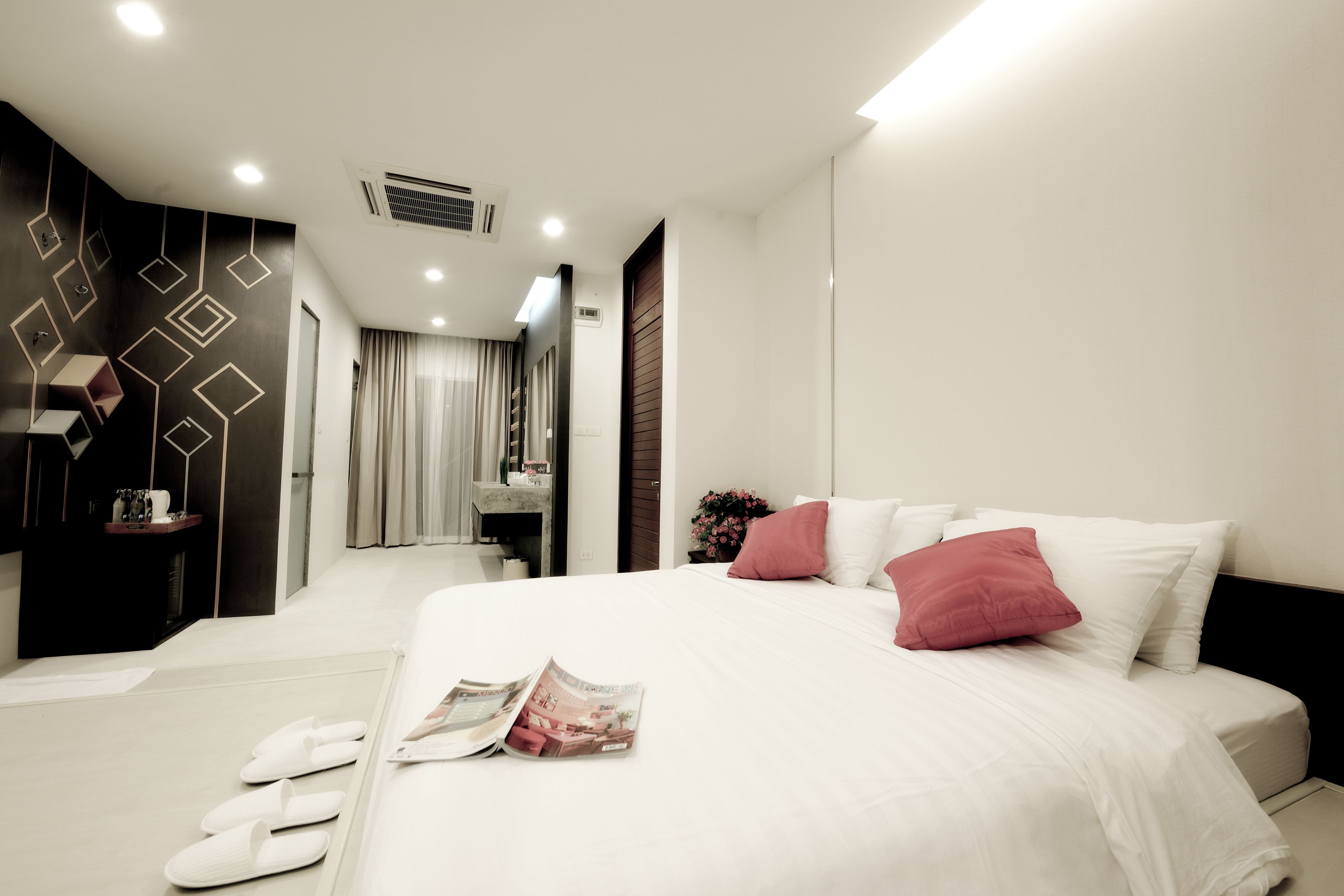 A modern hotel room with a large bed, a bedside table, a mirror, and a bathroom visible through an open door.
