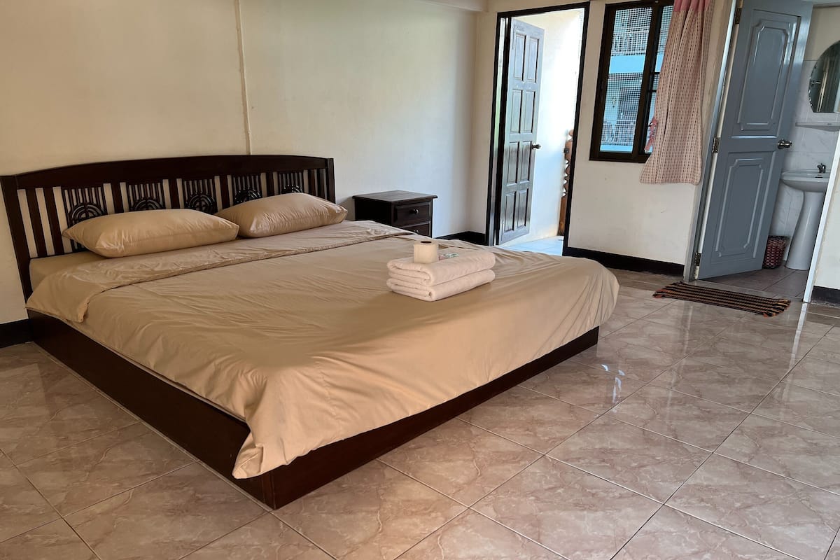 A neatly made bed with a beige bedspread and pillows, a small bedside table, and a bathroom visible through an open door.