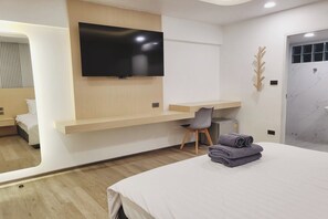 A modern hotel room with a flat-screen TV mounted on a wooden wall, a desk with a chair, a bed with a neatly folded towel, and a bathroom with a marble wall. - Sripoom House 1 (Chiang Mai)