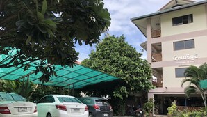 En hotelindgang med et overdækket parkeringsområde, en bygning med skiltet "SRIPOOM HOUSE" og flere krukker med planter.