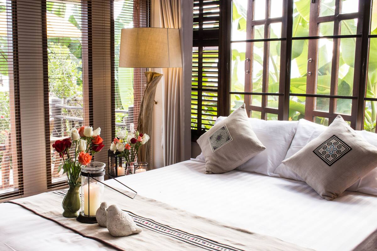 A bedroom with a bed, pillows, a vase with flowers, a candle, and a lamp.