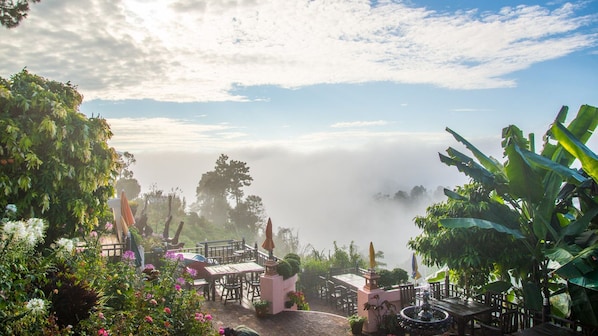 A garden with outdoor seating, a fountain, and a view of the sky and clouds.