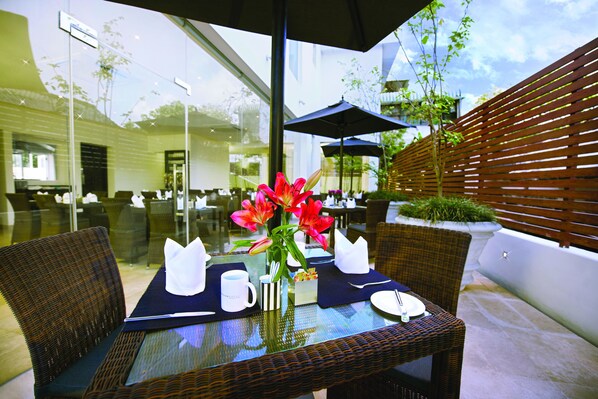 An outdoor dining area with wicker chairs, a glass table, and a vase of flowers. - Fair View Hotel Colombo (Colombo)