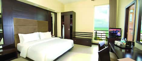 Habitación de hotel con una cama grande, un escritorio con televisor y un balcón con vistas.