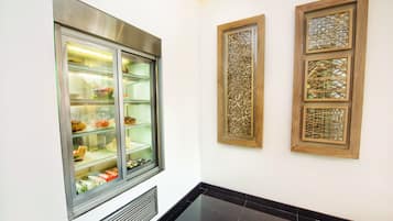 A corridor with a display case containing food items, a vent on the wall, and three framed decorative panels.