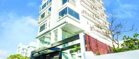 A modern hotel with a prominent glass entrance, multiple floors, and a clear sky.