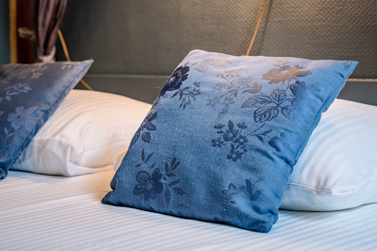 Una cama con dos almohadas, una lámpara roja y una pared con textura.