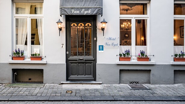 A building with a black door labeled "Van Eyck Hotel," featuring a classic design with a small balcony and potted plants. - Hotel Van Eyck (Bruges)