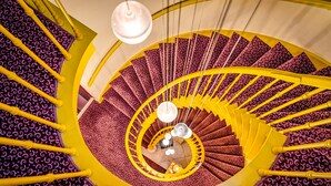A spiral staircase with yellow handrails and a patterned carpet. - Hotel Van Eyck (Bruges)