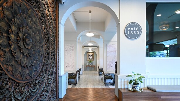 A hallway with a wooden herringbone floor, a decorative wall panel, a dining area with a table and chairs, and a sign reading "café 1860".