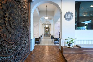 Un couloir doté d’un parquet en bois disposé en motif « point de Hongrie�», d’un panneau décoratif mural, d’un coin repas avec une table et des chaises, et d’une enseigne indiquant « café 1860 ».
