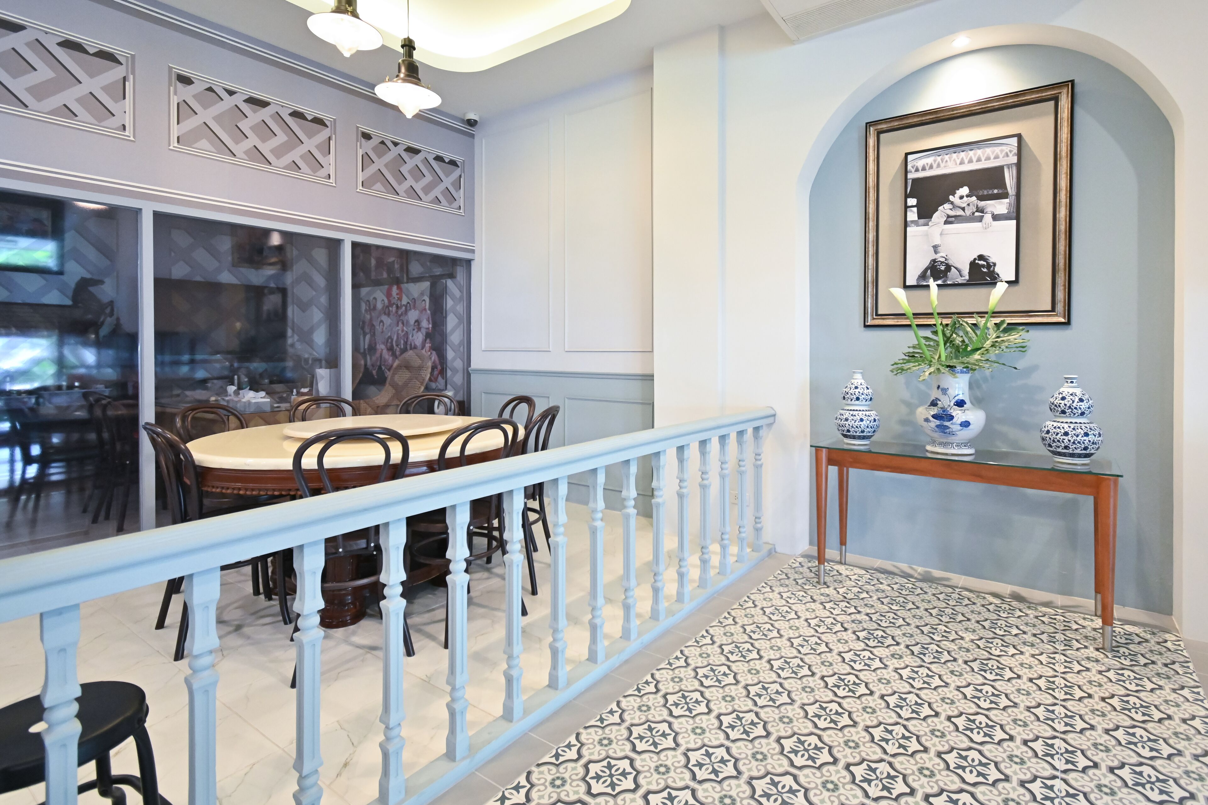 A dining area with a round table and chairs, a blue railing, and a patterned floor.