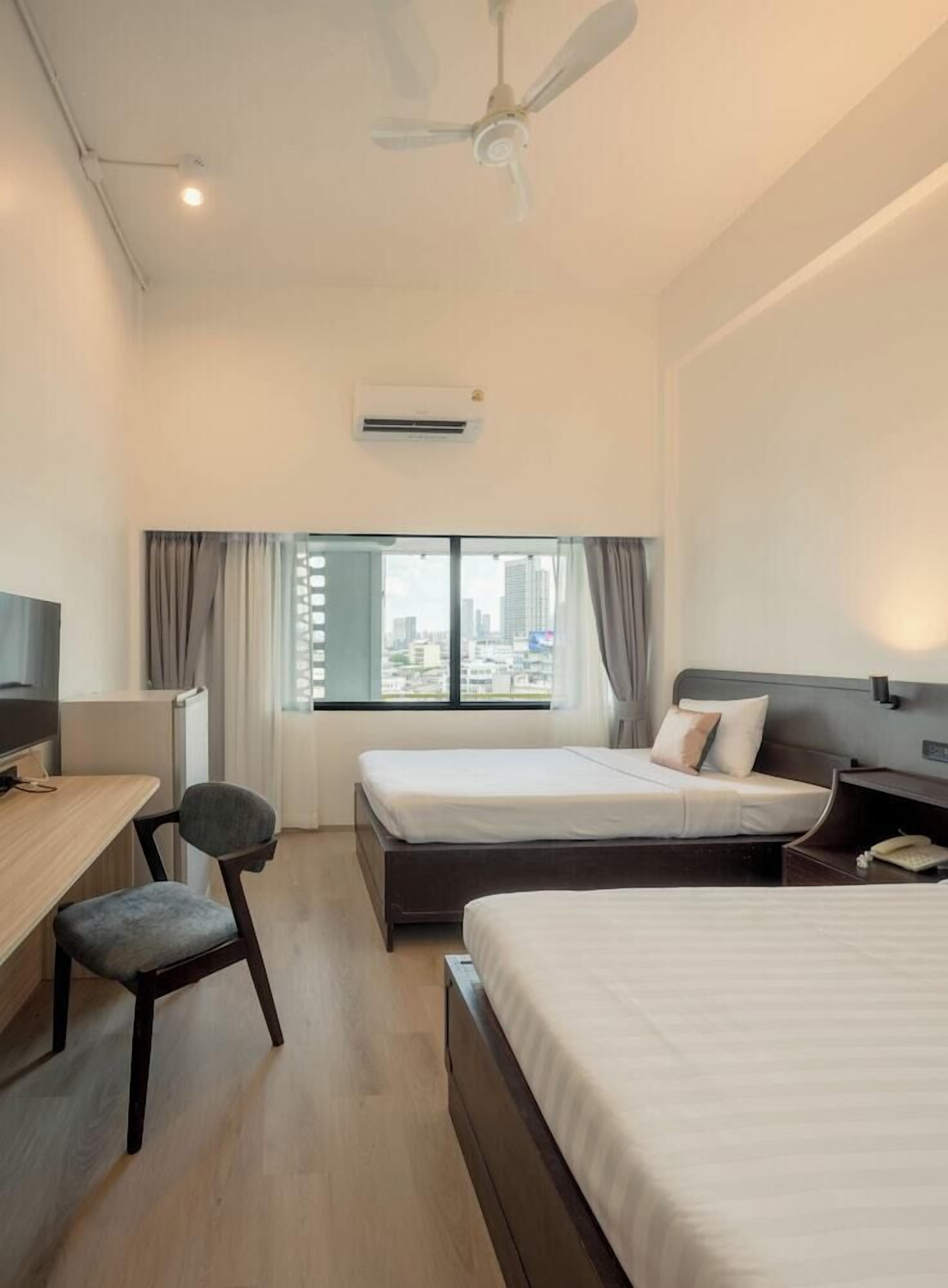 Hotelkamer met twee bedden, een bureau, een stoel, een airconditioner en uitzicht over de stad.