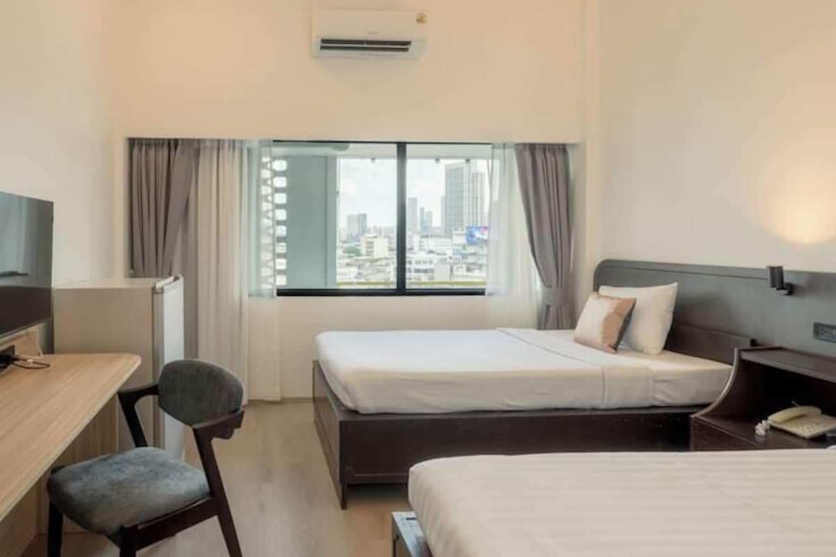 A hotel room with two beds, a desk, a chair, an air conditioning unit, and a city view.