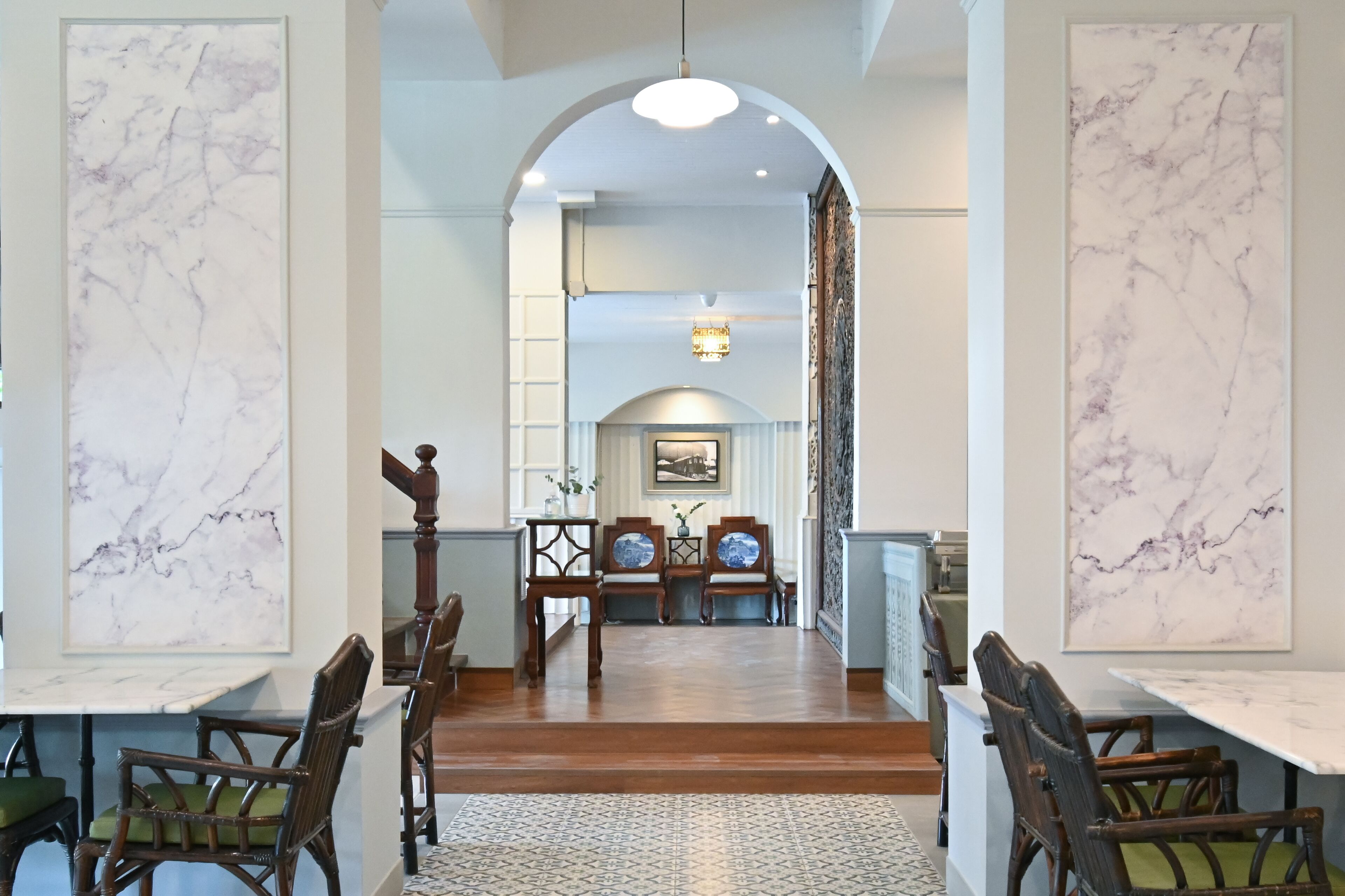 A dining area with a marble wall, wooden chairs, a central table, and a chandelier.
