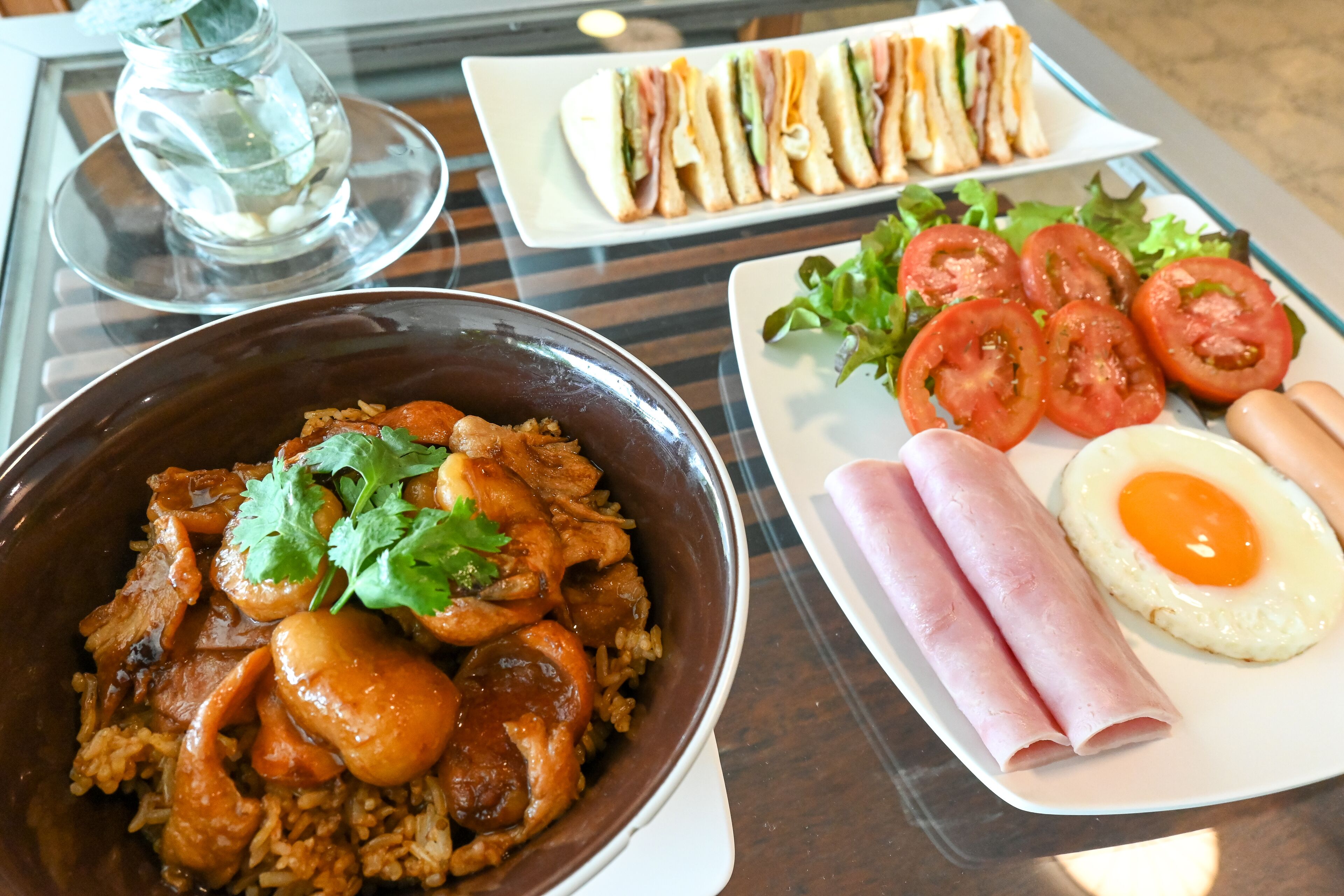 A table with a variety of dishes including a bowl of rice with meat, a plate of sandwiches, and a plate with eggs and vegetables.