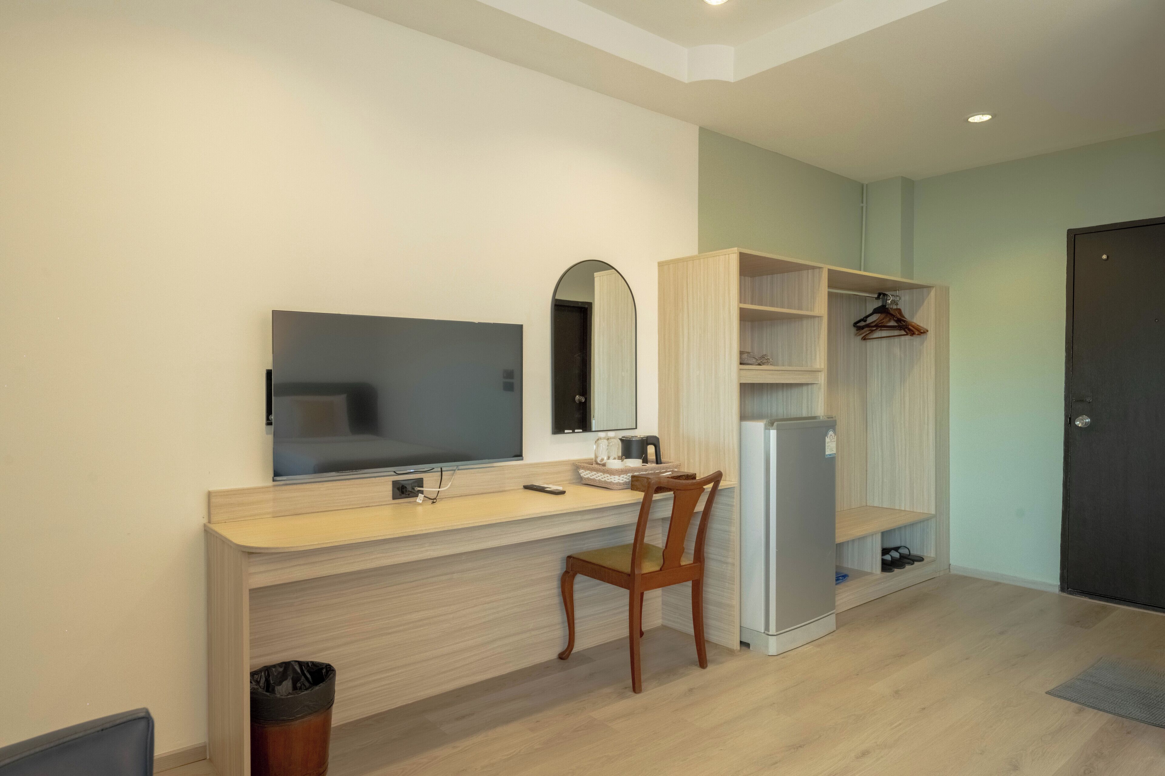 A modern, well-lit room with a wooden desk, a chair, a flat-screen TV, a mirror, a wardrobe, and a door.