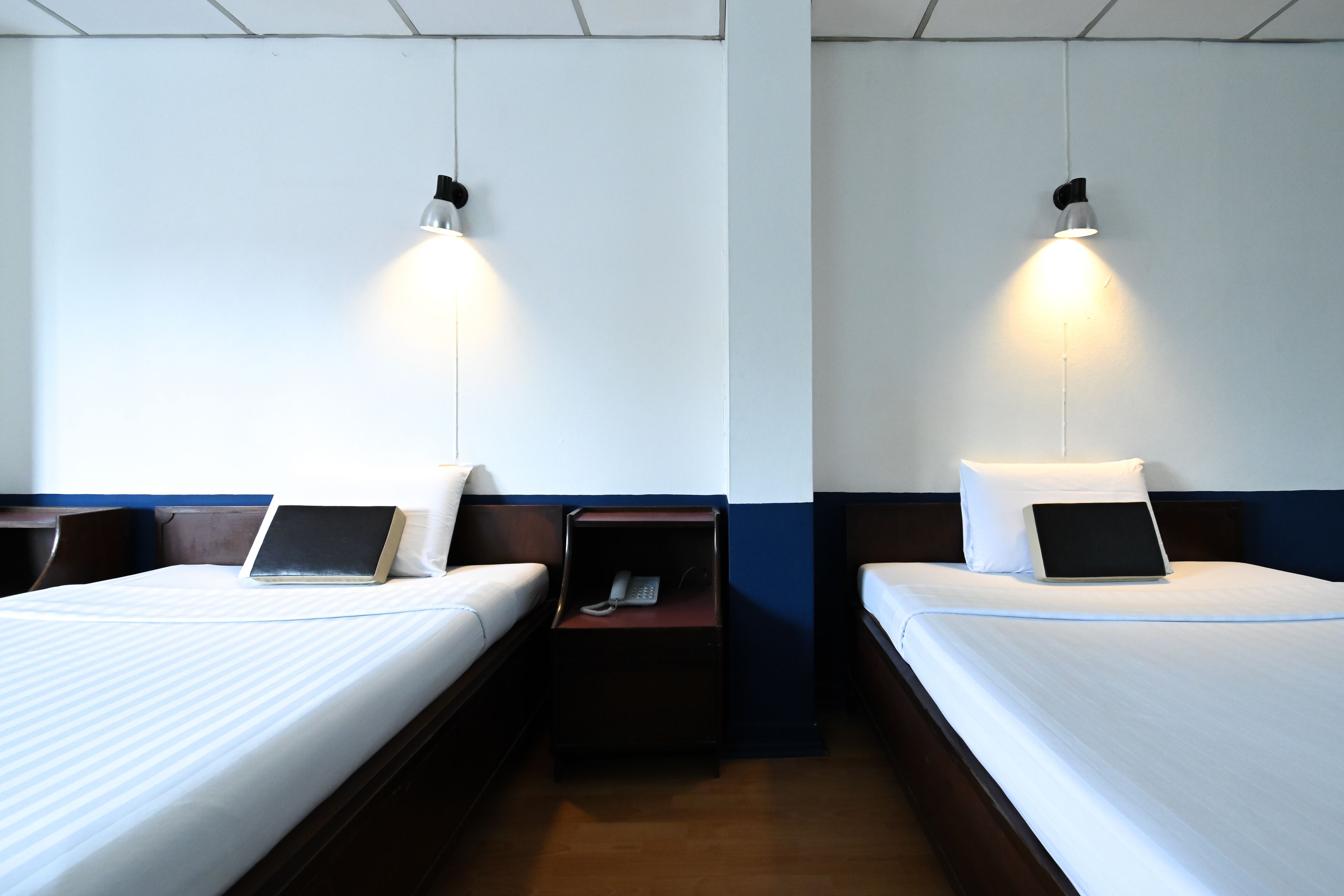 Deux lits simples avec du linge de lit blanc, des tables de chevet avec des lampes et une petite table de nuit avec un téléphone.