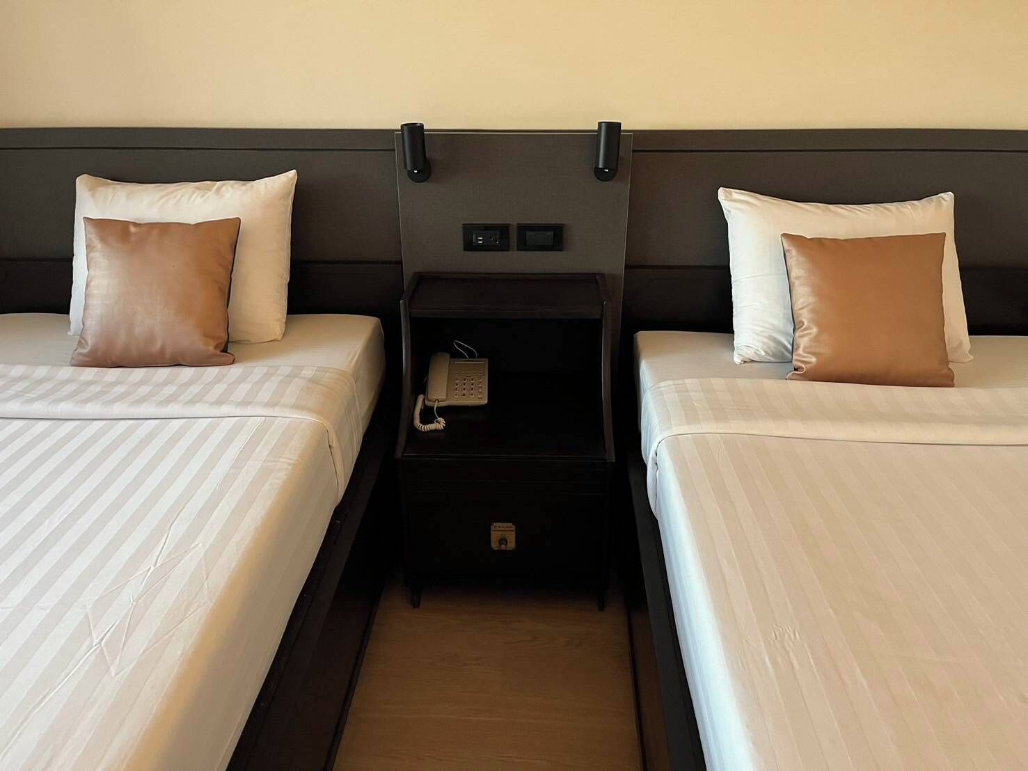 Habitación de hotel con dos camas, cada una con una almohada y una mesita de noche con teléfono.