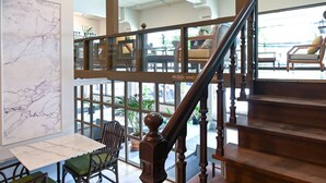 A hotel lobby with a marble wall, a staircase, and a seating area with chairs and tables.