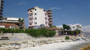 Un edificio costero con balcones, un muro de piedra y una playa al frente.